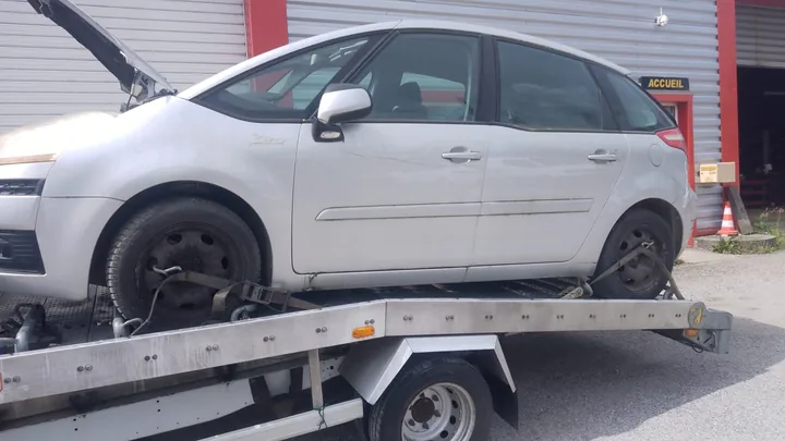 Monospace blanc au capot ouvert, avec des retenues près des roues sur un plateau.