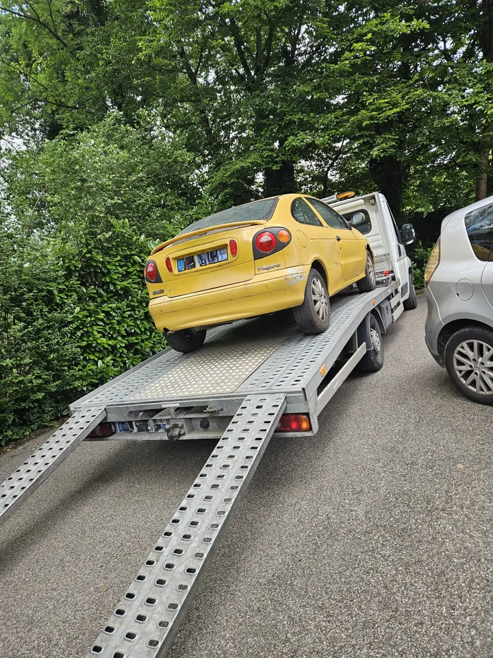 Coupé jaune sur une dépanneuse avec deux rampes abaissées près d’une voiture.