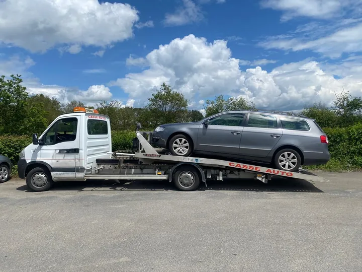 Voiture grise allongée installée sur un camion plateau blanc en extérieur.