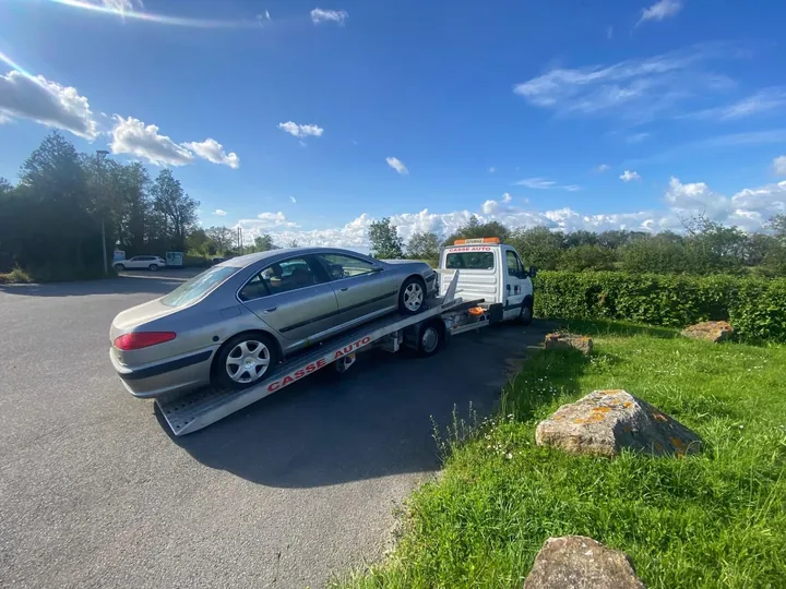 Berline grise sur une dépanneuse au plateau abaissé près d’une haie.