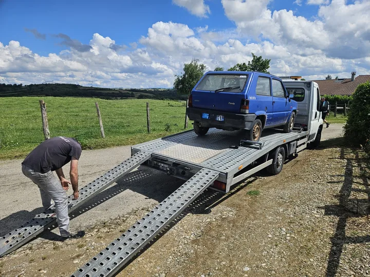 Personne penchée près des rampes d’une dépanneuse portant une petite voiture bleue.