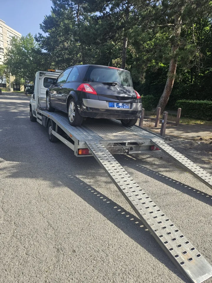 Citadine sur une dépanneuse avec la rampe descendue dans une rue ombragée.