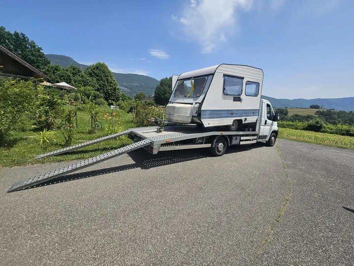 Camion plateau et utilitaire clair sur une route avec des rampes déployées.