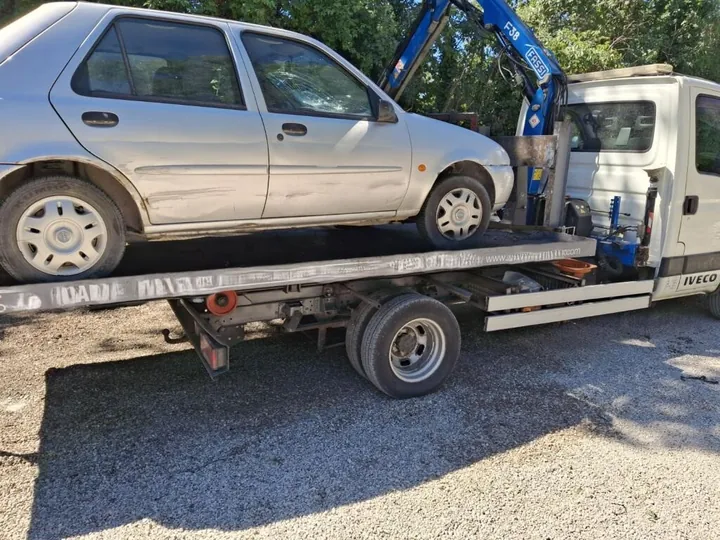 Citadine grise aux portes et bas de caisse rayés sur une dépanneuse à grue.