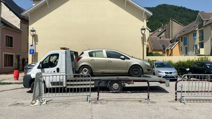 Citadine claire sur une dépanneuse à proximité de barrières métalliques.
