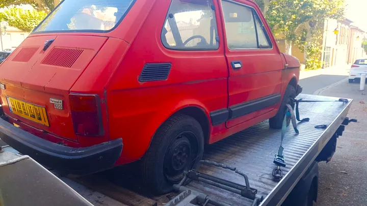 Petite voiture rouge ancienne avec des sangles sur un plateau de dépanneuse.