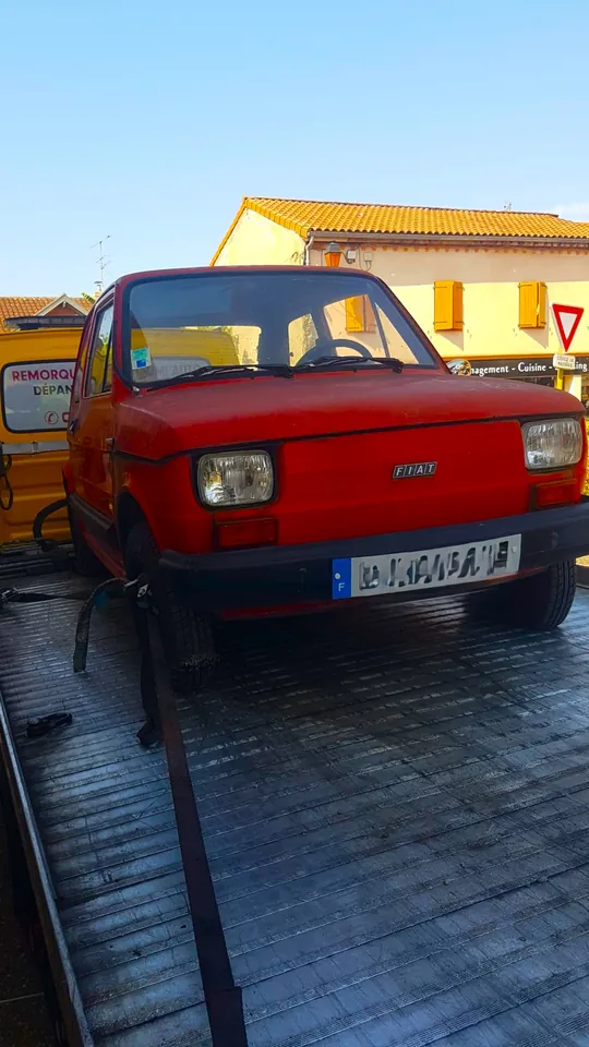 Avant d’une petite Fiat rouge sur un plateau, avec une sangle dirigée vers une roue.