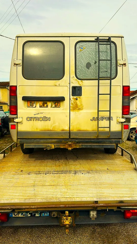 Arrière d’un fourgon blanc avec une échelle, chargé sur une dépanneuse.