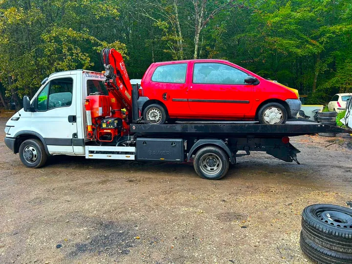 Voiture rouge sur le plateau d’un camion blanc équipé d’une grue rouge.