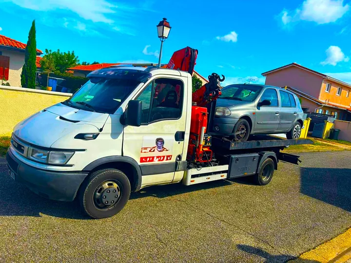 Citadine claire sur une dépanneuse à grue dans une rue bordée de maisons.