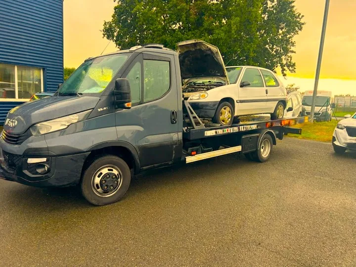 Petite voiture claire au capot ouvert sur une dépanneuse grise.