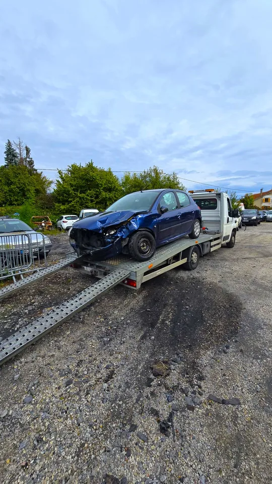Citadine bleue au capot et à l’avant déformés sur une dépanneuse avec rampes.