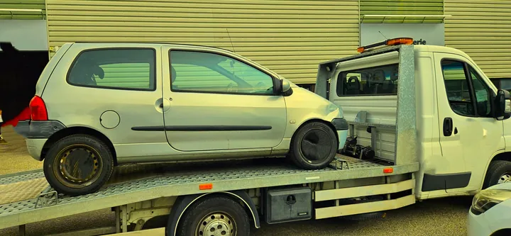 Petite voiture blanche transportée de profil sur une dépanneuse.