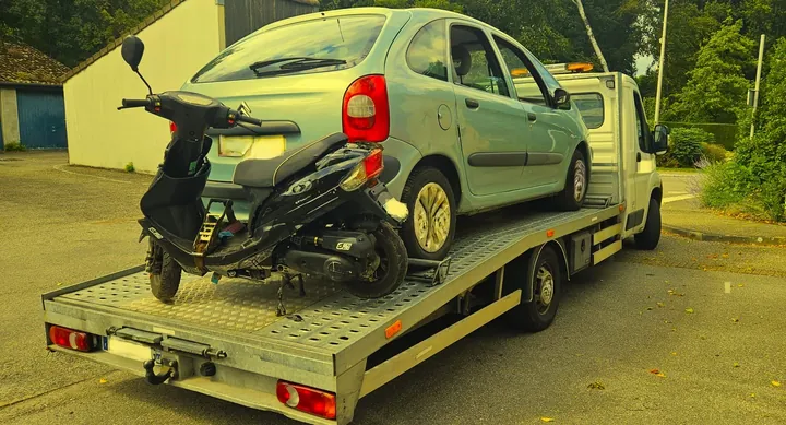 Petite voiture claire et deux-roues visibles sur un plateau de transport.
