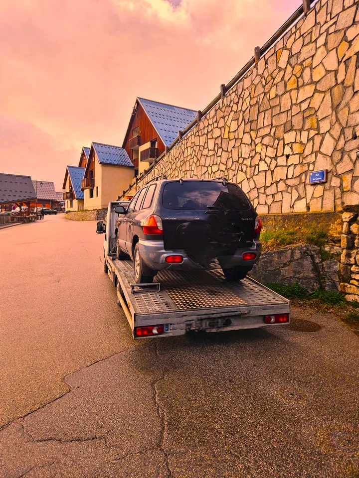 Vue arrière d’une dépanneuse transportant une voiture sombre dans une rue de village.