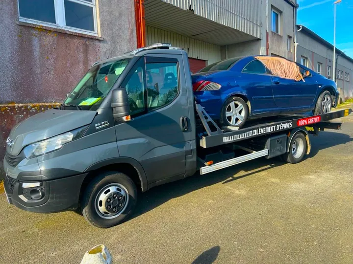 Coupé bleu installé sur une dépanneuse sombre devant un bâtiment.