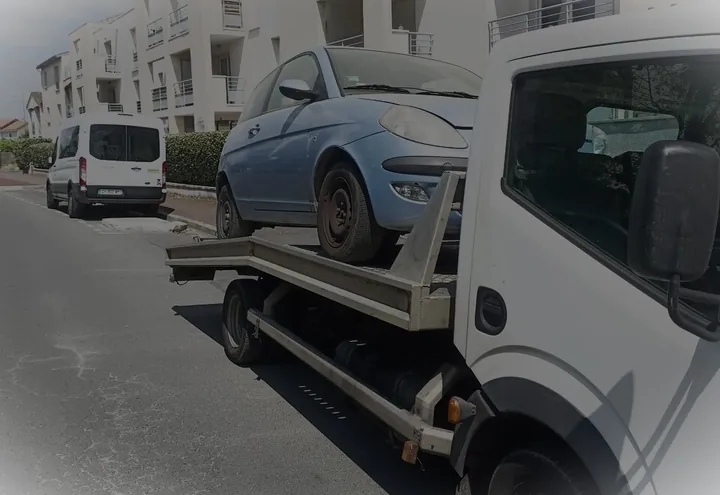 Voiture bleue installée sur le plateau d’une dépanneuse blanche dans une rue urbaine.