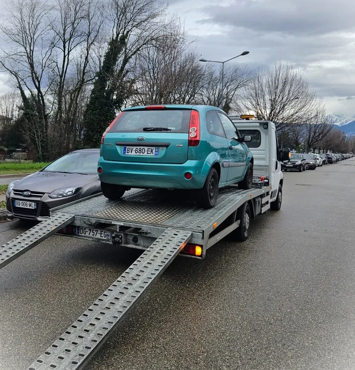 Arrière d’une citadine turquoise sur un plateau de transport avec une rampe descendue.