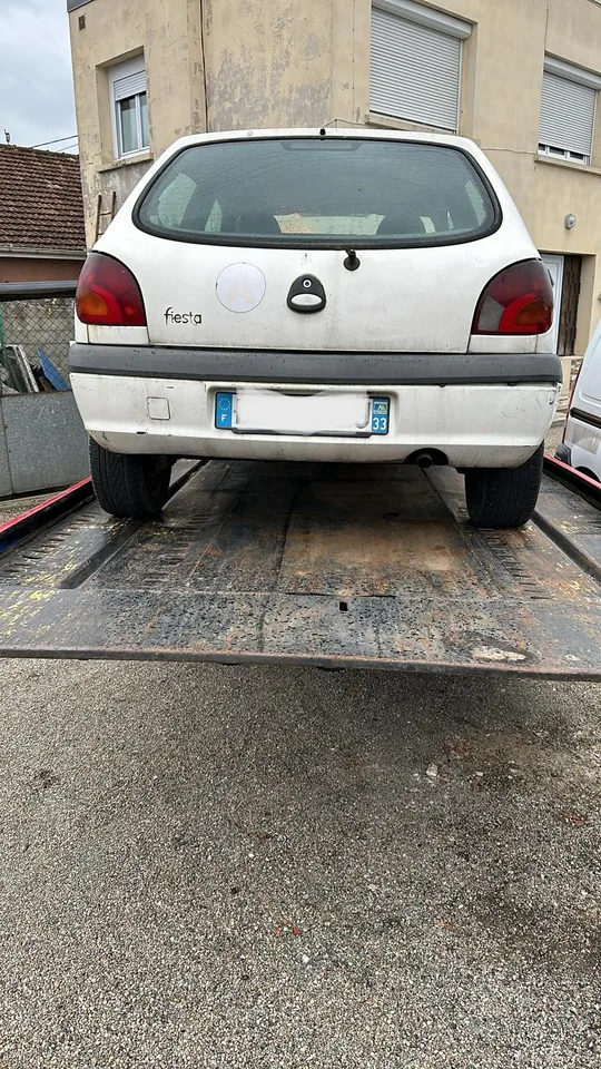 Arrière d’une petite voiture blanche sur un plateau métallique.