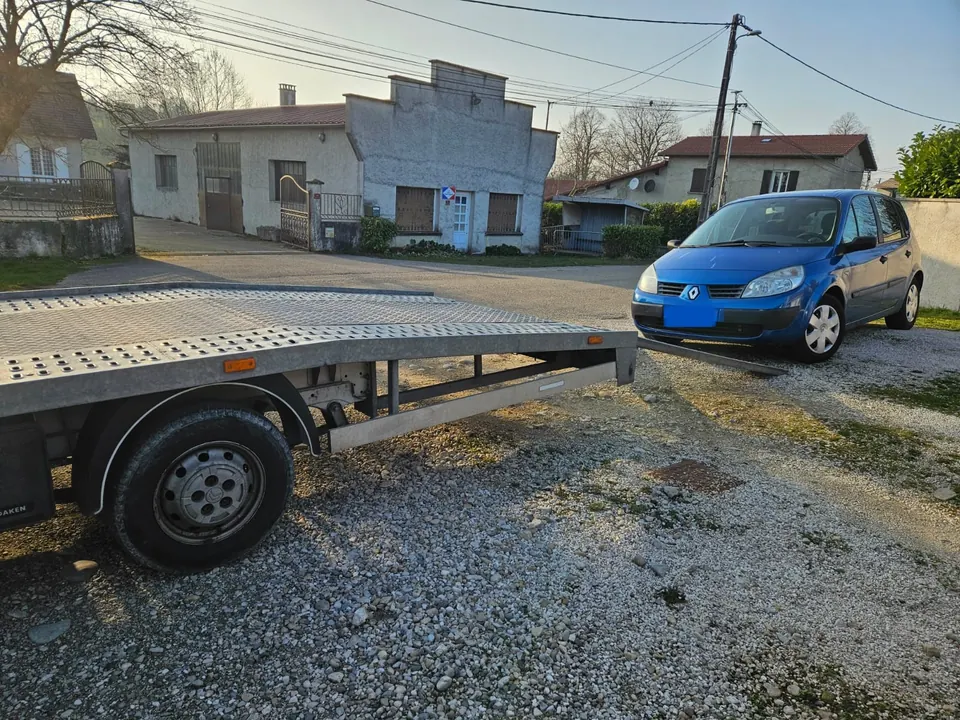 Voiture bleue devant les rampes déployées d’un camion plateau.