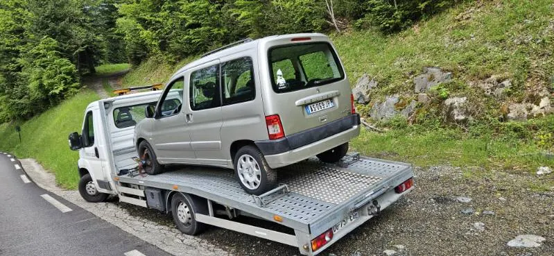 Véhicule clair à carrosserie haute installé sur un camion plateau blanc.