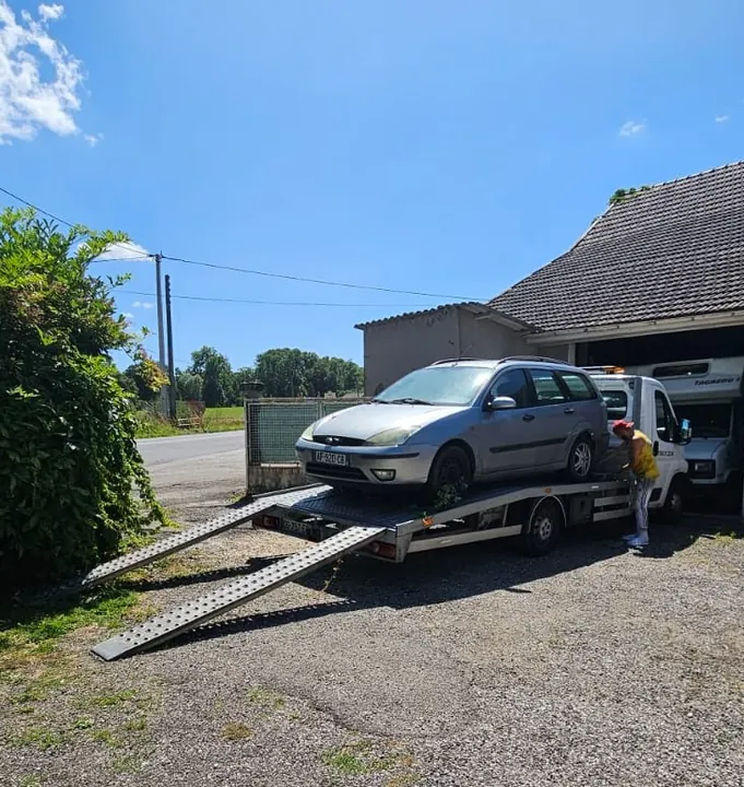 Voiture claire près d’un camion plateau dans une entrée bordée de végétation.