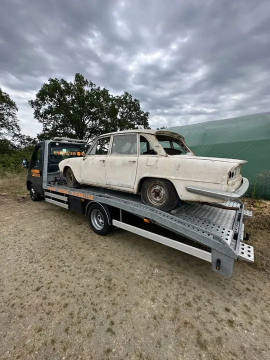 Voiture ancienne de couleur claire installée sur le plateau d’un camion.