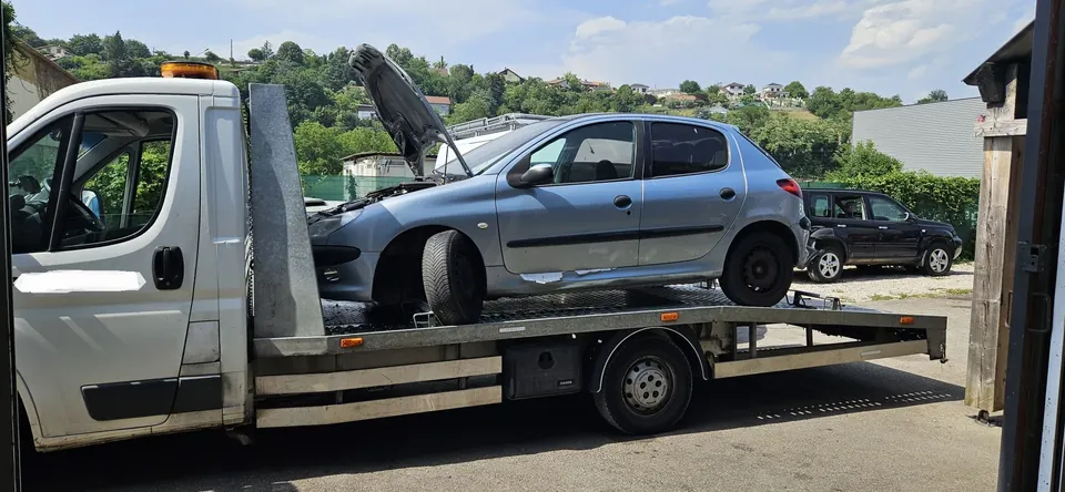 Voiture claire sur le plateau d’un camion blanc, avec la cabine à gauche.