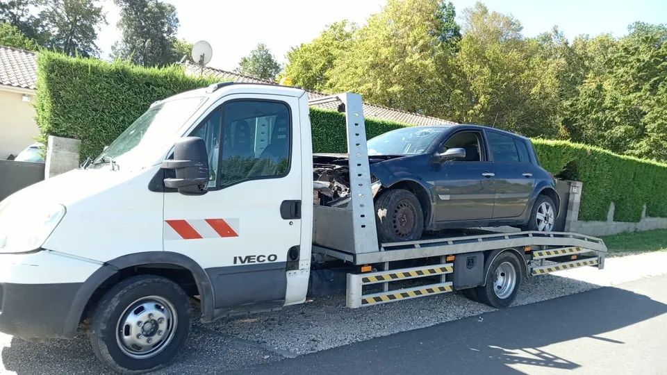 Voiture bleue installée sur le plateau d’un camion blanc.