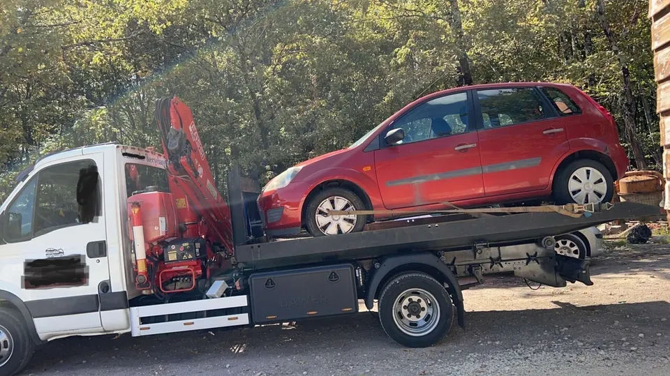 Voiture rouge sur le plateau d’un camion blanc équipé d’une grue repliée.