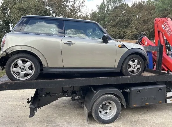 Petite voiture claire sur le plateau d’un camion équipé d’une grue rouge.