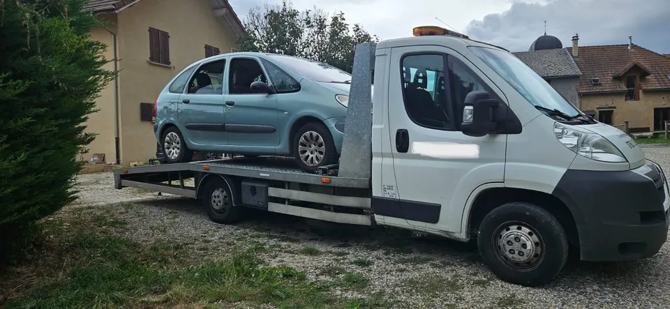 Camion blanc portant une voiture verte devant une habitation.